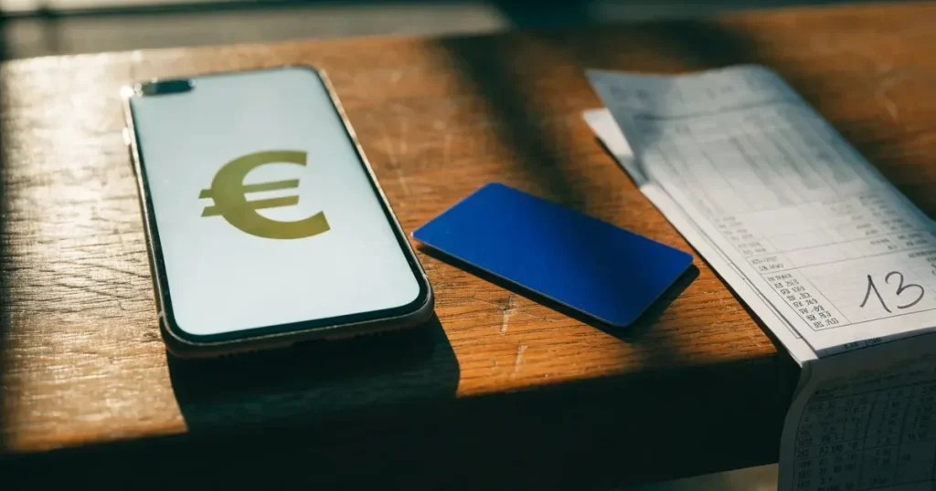 Uno smartphone e una carta di pagamento affiancati su un tavolo di legno, con alcune banconote da euro accanto